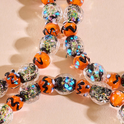 NOGU Carnival of Shadows pumpkin beaded bracelet with orange glass beads, black swirls, and iridescent metallic accents.