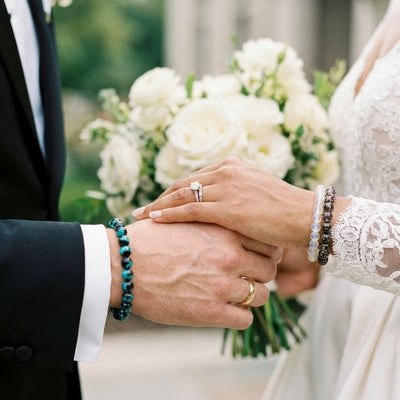 NOGU Wedding Edit handcrafted beaded bracelets in teal, white and black worn by a bride and groom holding hands.
