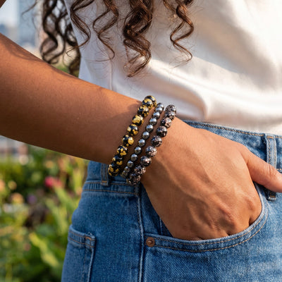 NOGU Made to Pair Obsidian Firefly Glass beaded bracelets, stacked in black, gold, and metallic gray on a wrist.