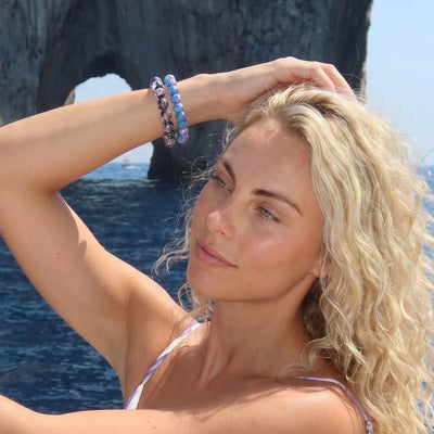 Model wearing NOGU Made to Pair Hyacinth Firefly Glass and diamond-shimmer beaded bracelets in purple and blue.