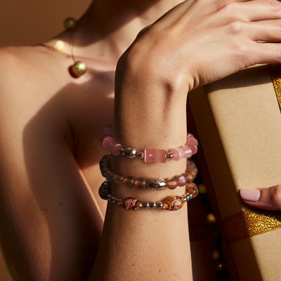 NOGU Gifts That Feel Expensive collection features stacked pink beaded bracelets with silver-tone accents beside a wrapped gift.