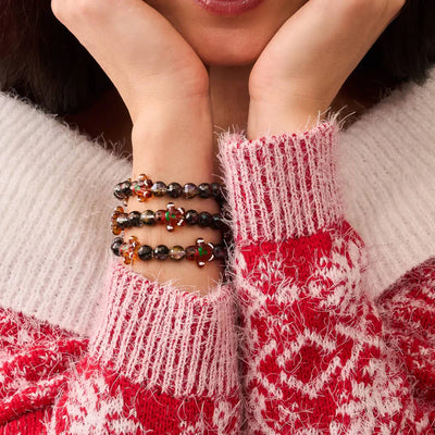 NOGU Vault Christmas bracelets with dark faceted beads and gingerbread charms, styled with a red-and-white knit sweater.