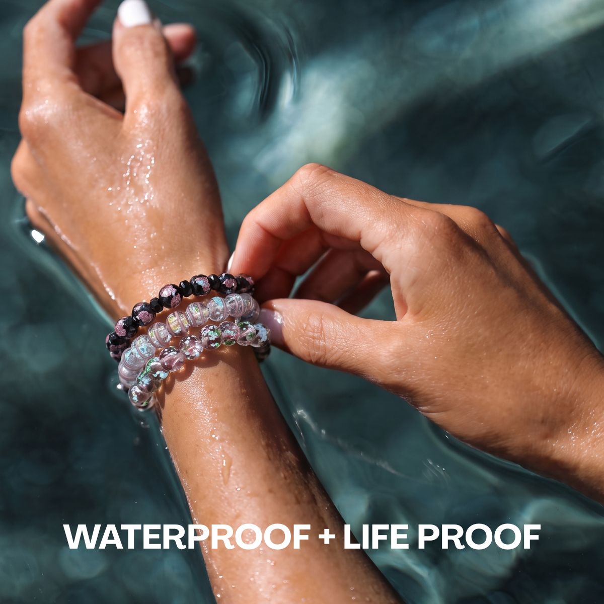 Stacked waterproof beaded bracelets in iridescent clear, pink, green and black beads worn in water.
