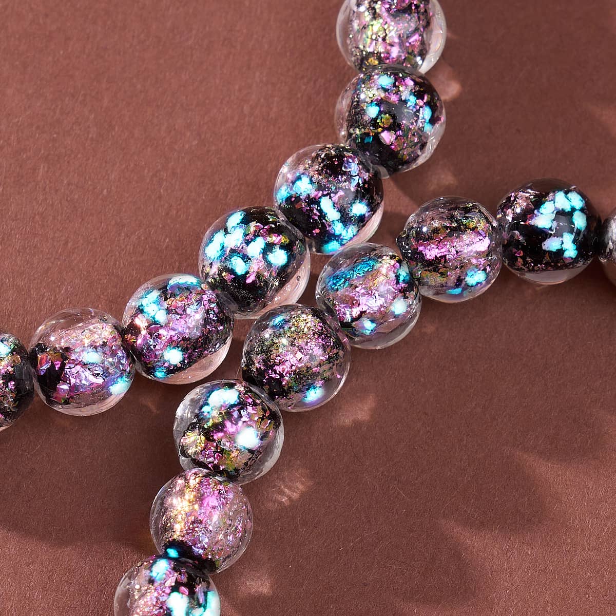 Violet Potion Firework Glass Neon Bracelet with clear round beads flecked in violet, pink, turquoise, and gold shimmer.