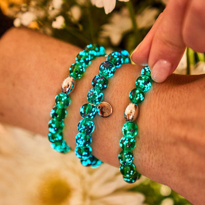Blue Shamrock Firefly Glass bracelets glowing turquoise with silver charm beads on wrist by NOGU