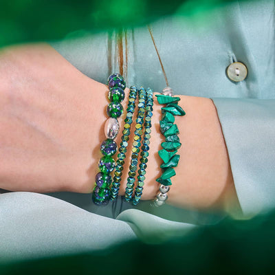 Blue Shamrock Firefly Glass bracelet with green and blue beads alongside silver and malachite bracelets on wrist by NOGU