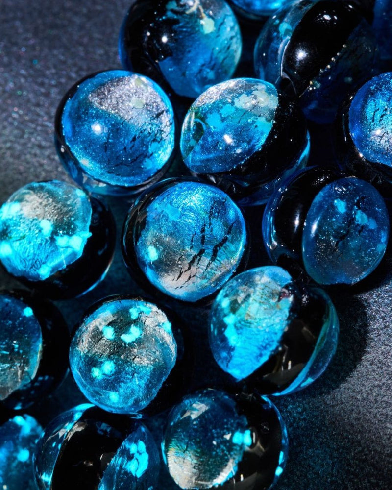 Glossy cobalt blue glass spheres with shimmering silver flecks, a celestial-inspired NOGU jewelry brand creative.