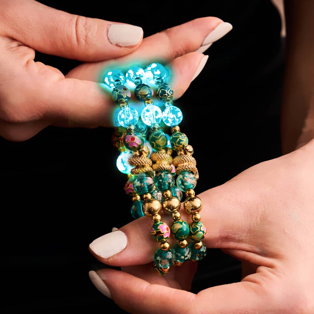 Sea Dragon teal firefly glass and enamel lotus serpent bracelet with 18k gold beads held in hands by NOGU