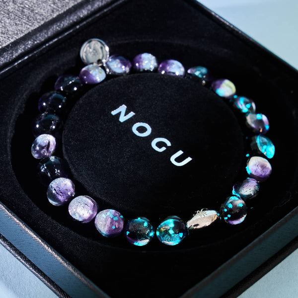 Violet Moon bracelet with color-shifting lunar glass beads and 18k white gold sterling silver bead displayed in NOGU box
